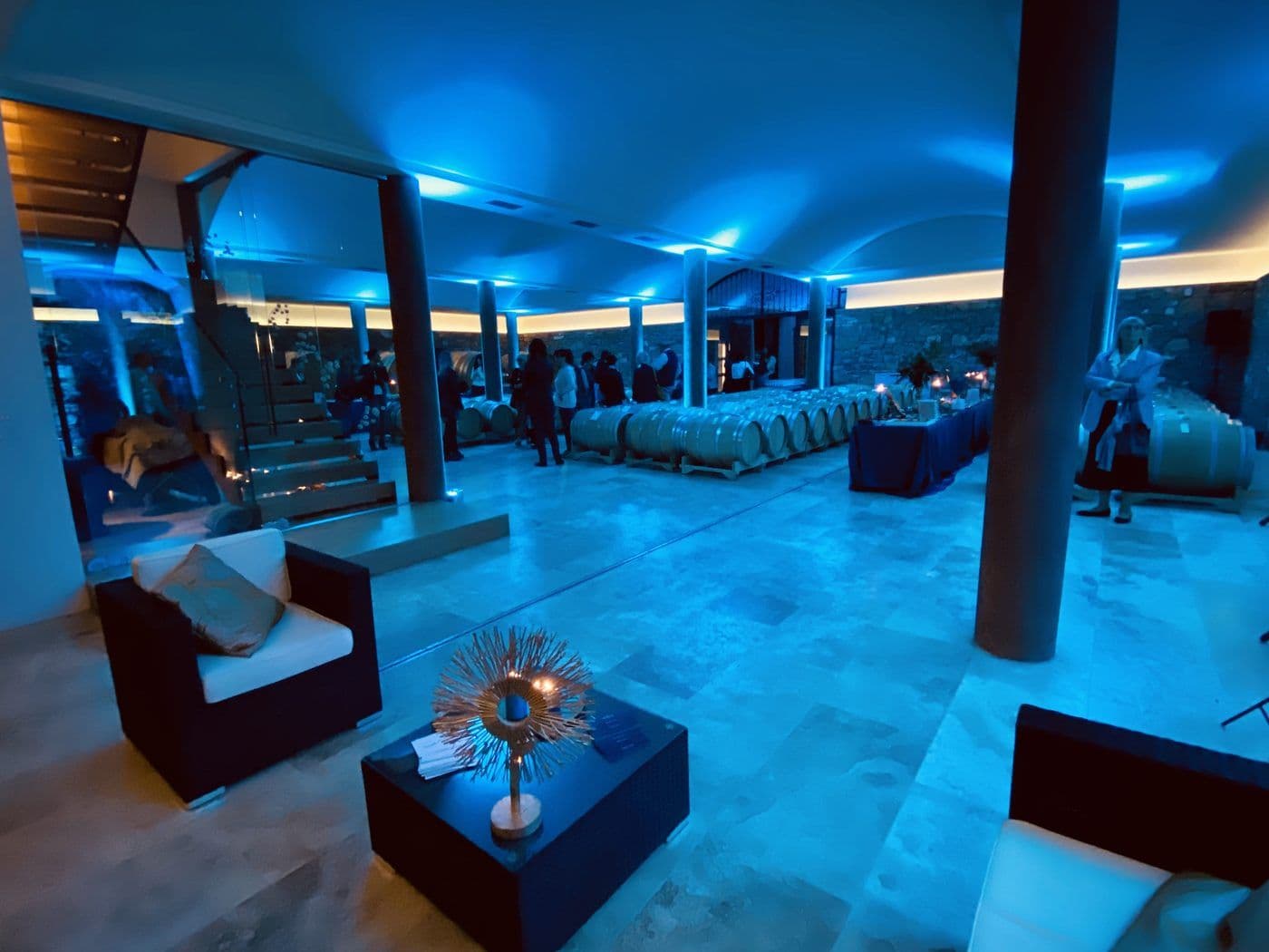 Cantina illuminata di blu con botti e ospiti durante un evento